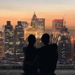 Silhouette of couple sit on ground point faraway on the roof above the city in the night.