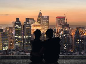 Silhouette of couple sit on ground point faraway on the roof above the city in the night.